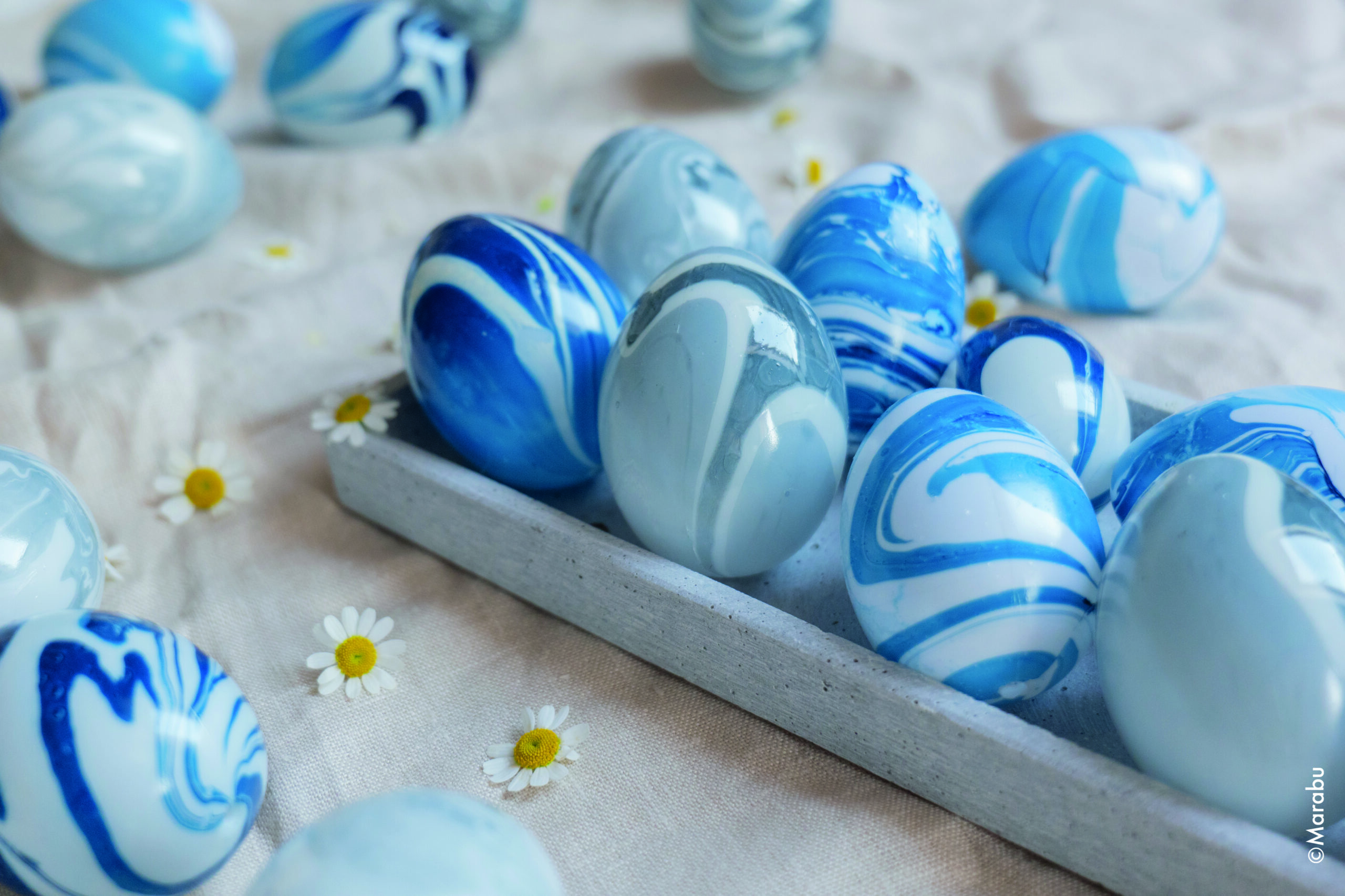 Blå marmorerte påskeegg ligger i et grått brett.
