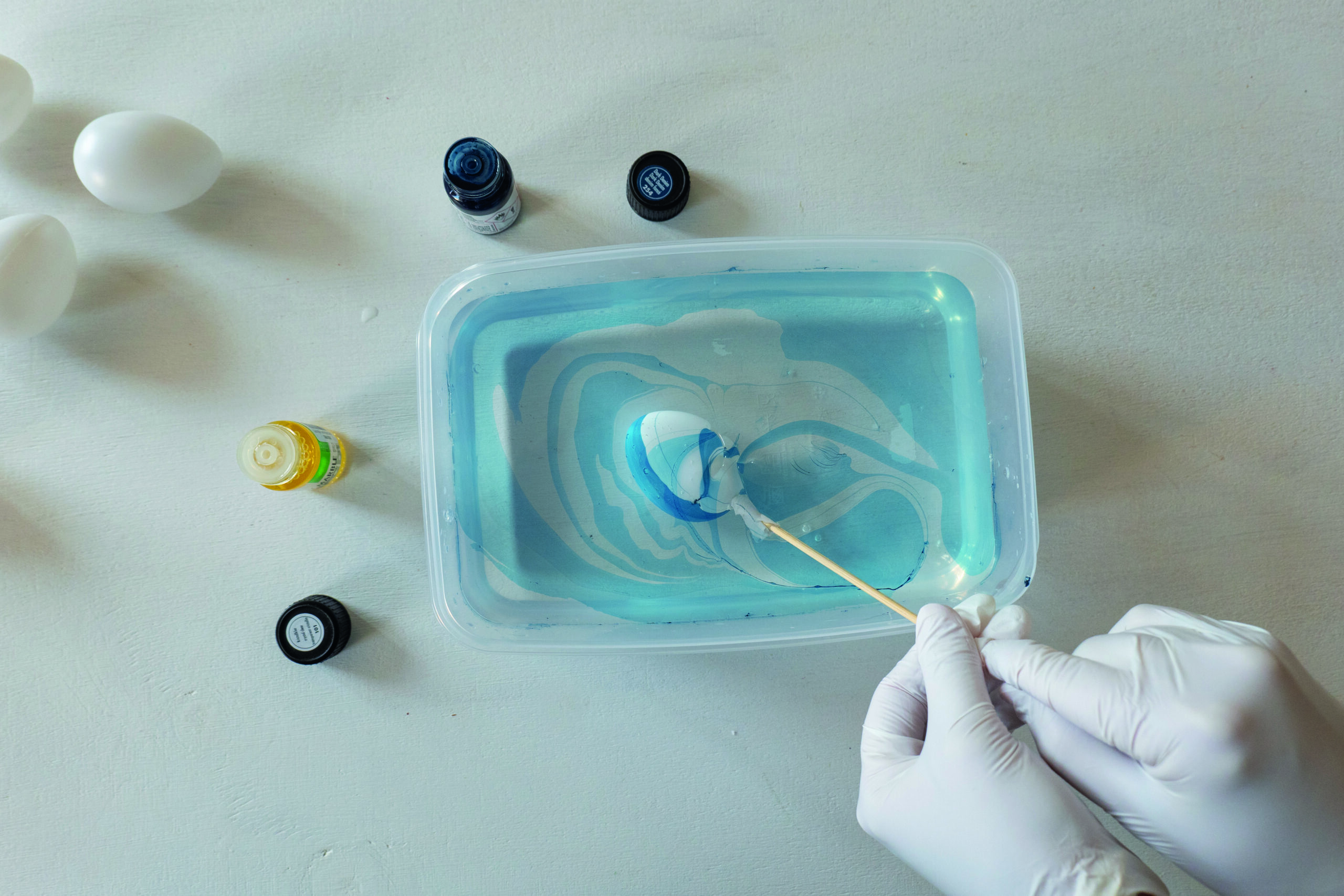 Egg holdes på pinne og dyppes i blått marmoreringsbad.
