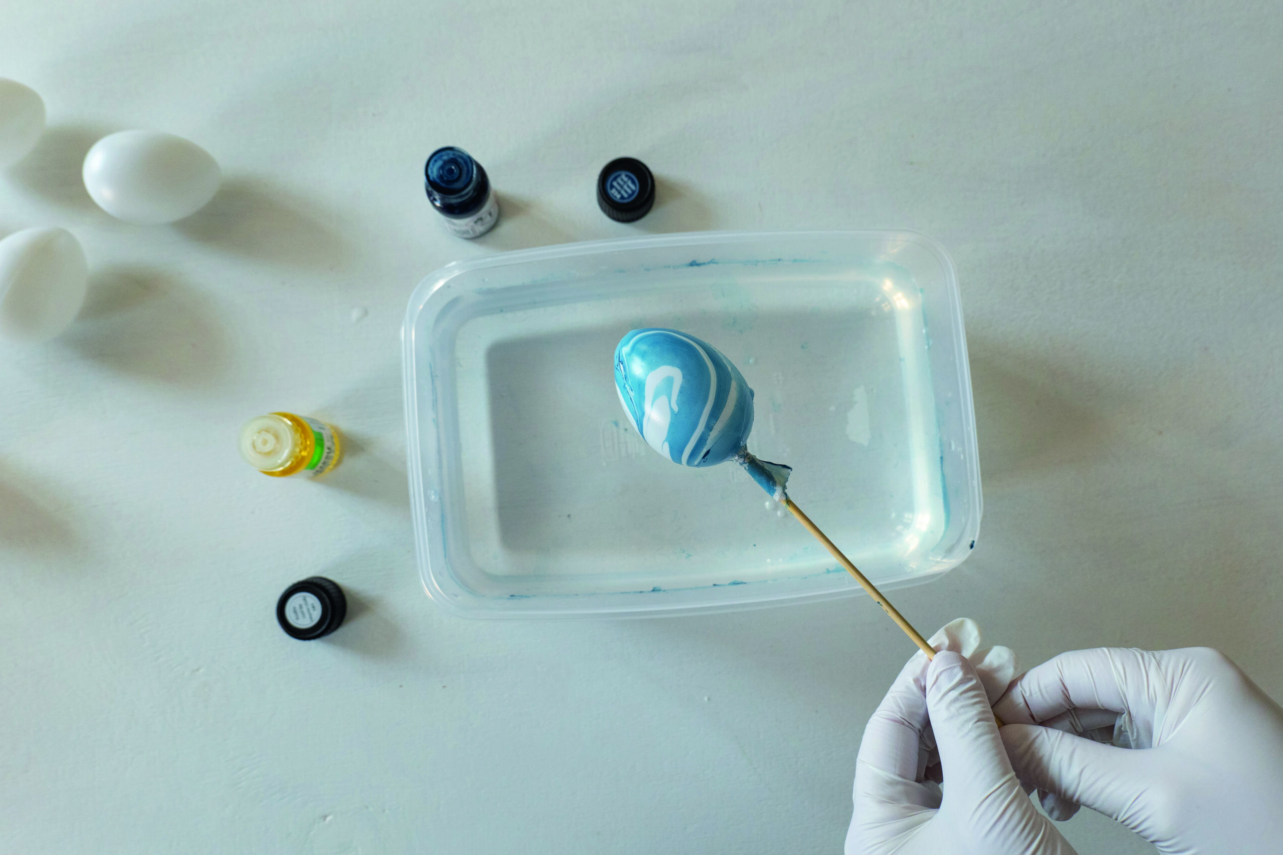 Egg med blått marmormønster holdes over plastboks med vann og marmoreringsfarge.