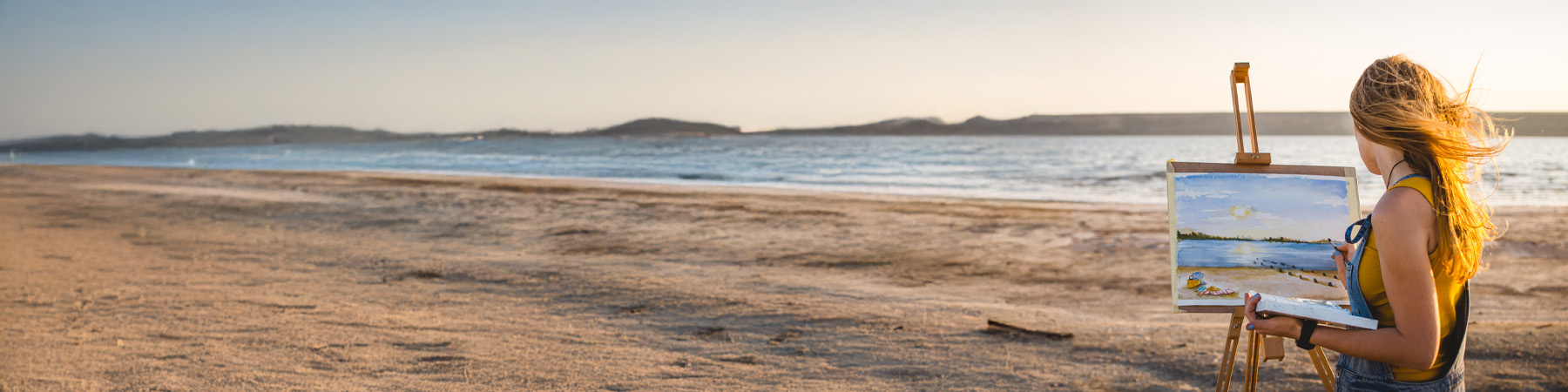 Kvinne som maler med akvarellmaling på et feltstaffeli på en strand