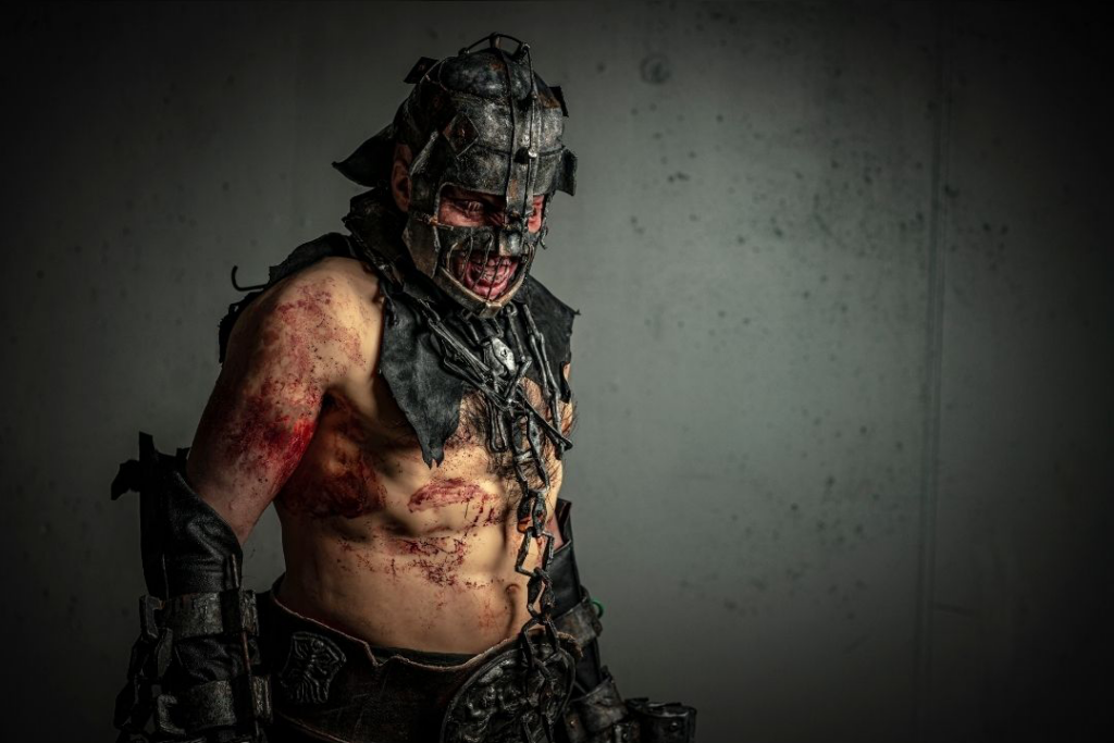 Cosplayer med hjelm og rustningsdeler sammen med et blodig utrykk gjort med SFX sminke.