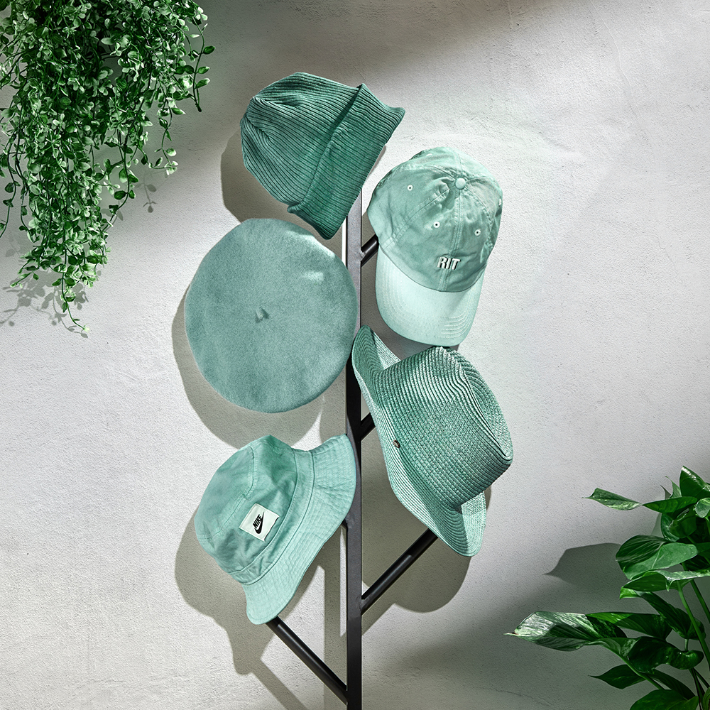 Fem mintgrønne hatter henger på et svart stativ mot lys vegg.
