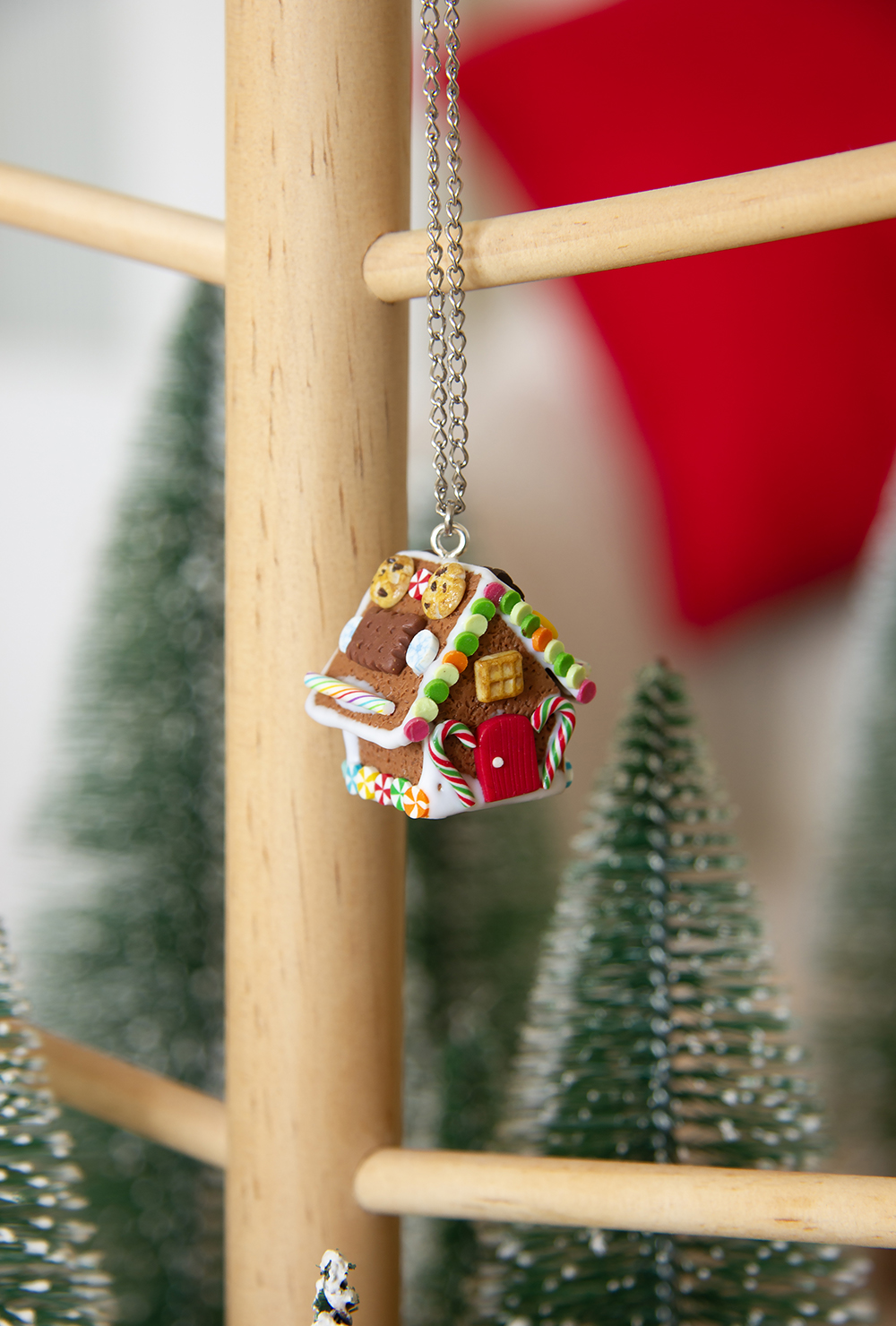 Cernit-miniatyr av pepperkakehus som henger i sølvkjede på trestativ.