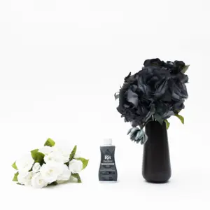 Ferdig fargede mørke blomster i en svart vase ved siden av hvite blomster og fargeflaske.
