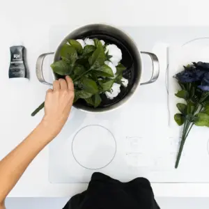 Hvite kunstige blomster senkes ned i svart fargebad i en kjele.