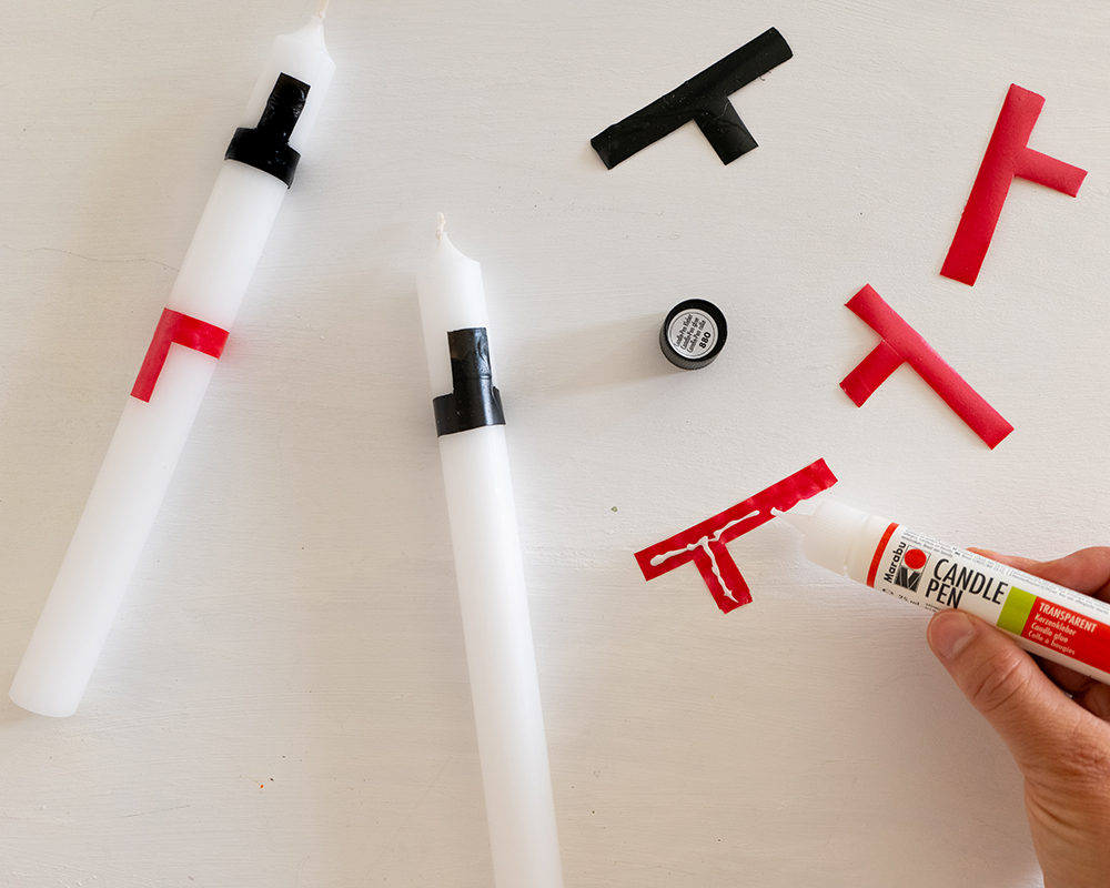 Hånd limer røde og svarte voksdeler på hvite lys med Candle Pen.