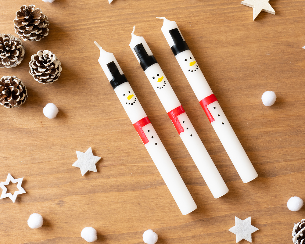 Tre hvite lys dekorert som snømenn med hatt, skjerf og ansikt malt på.