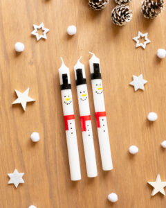 Tre hvite lys dekorert som snømenn med svarte hatter og røde skjerf.