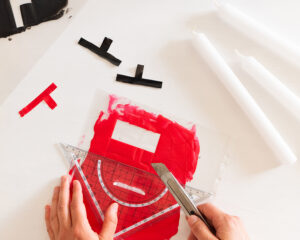 Hender bruker linjal og kuttekniv for å forme røde og svarte voksstykker.