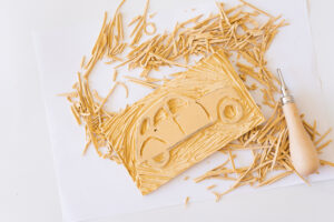 Linoplate med utskåret motiv av bil omgitt av skjærespon og linokniv.