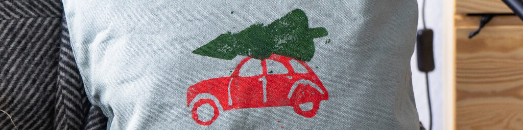 Grønn pute med rødt biltrykk og grønt juletre på toppen.