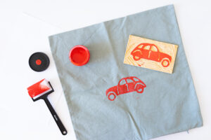 Rødt bilmotiv trykkes med linoplate på et stoffstykke.