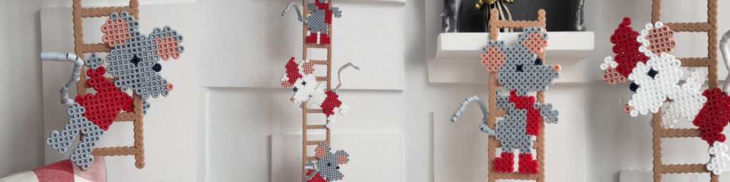 Flere Hama-perlemus i rødt, grått og hvitt klatrer på perlestiger mot lys vegg.