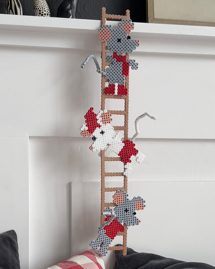 Perlede figurer av mus festet til en brun stige mot en hvit vegg.