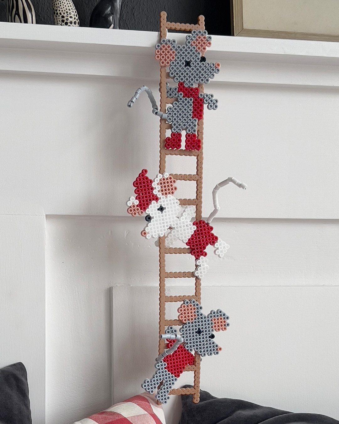 Perlede figurer av mus festet til en brun stige mot en hvit vegg.