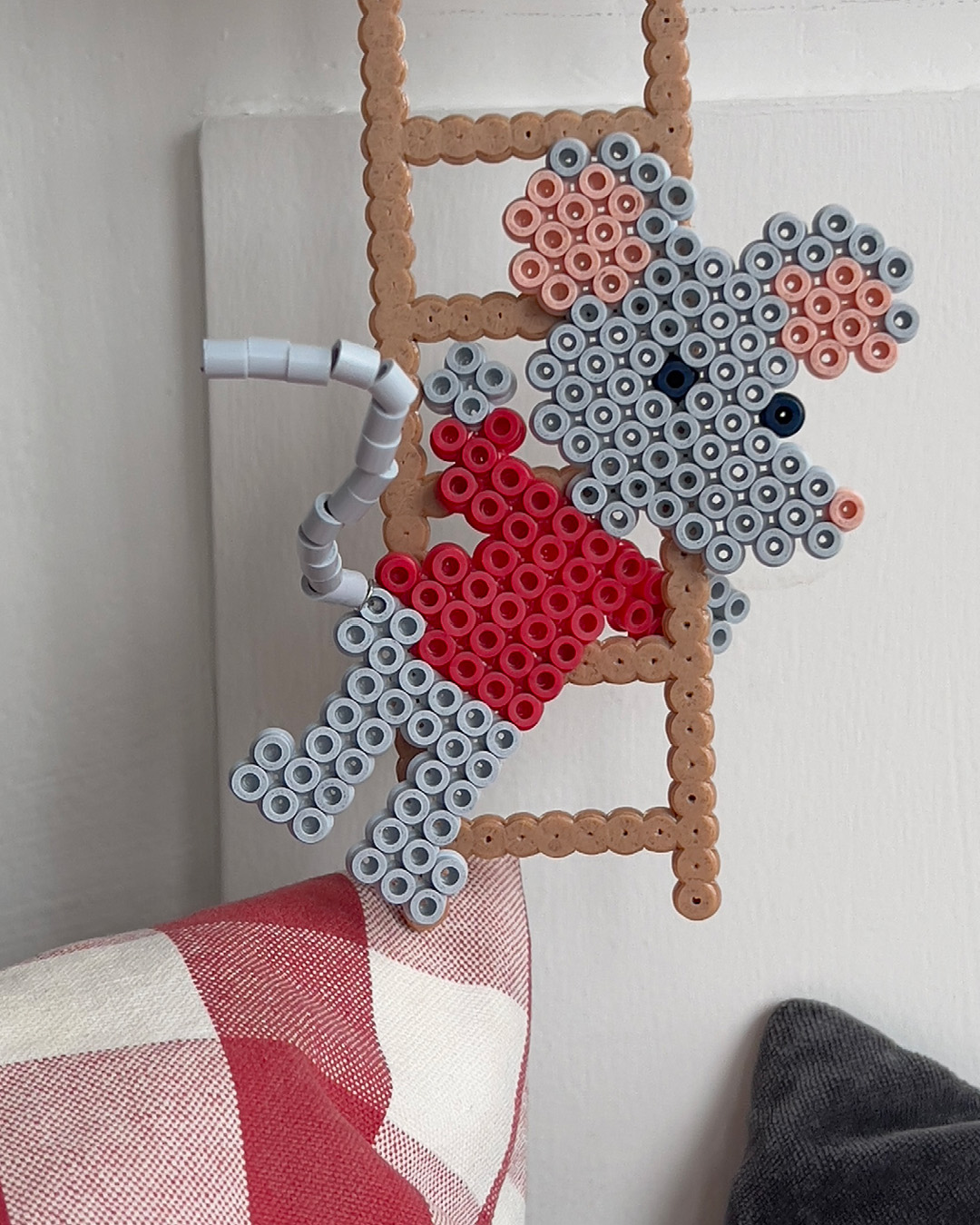 Hama-perlemus i rødt og grått henger på en brun perlestige.