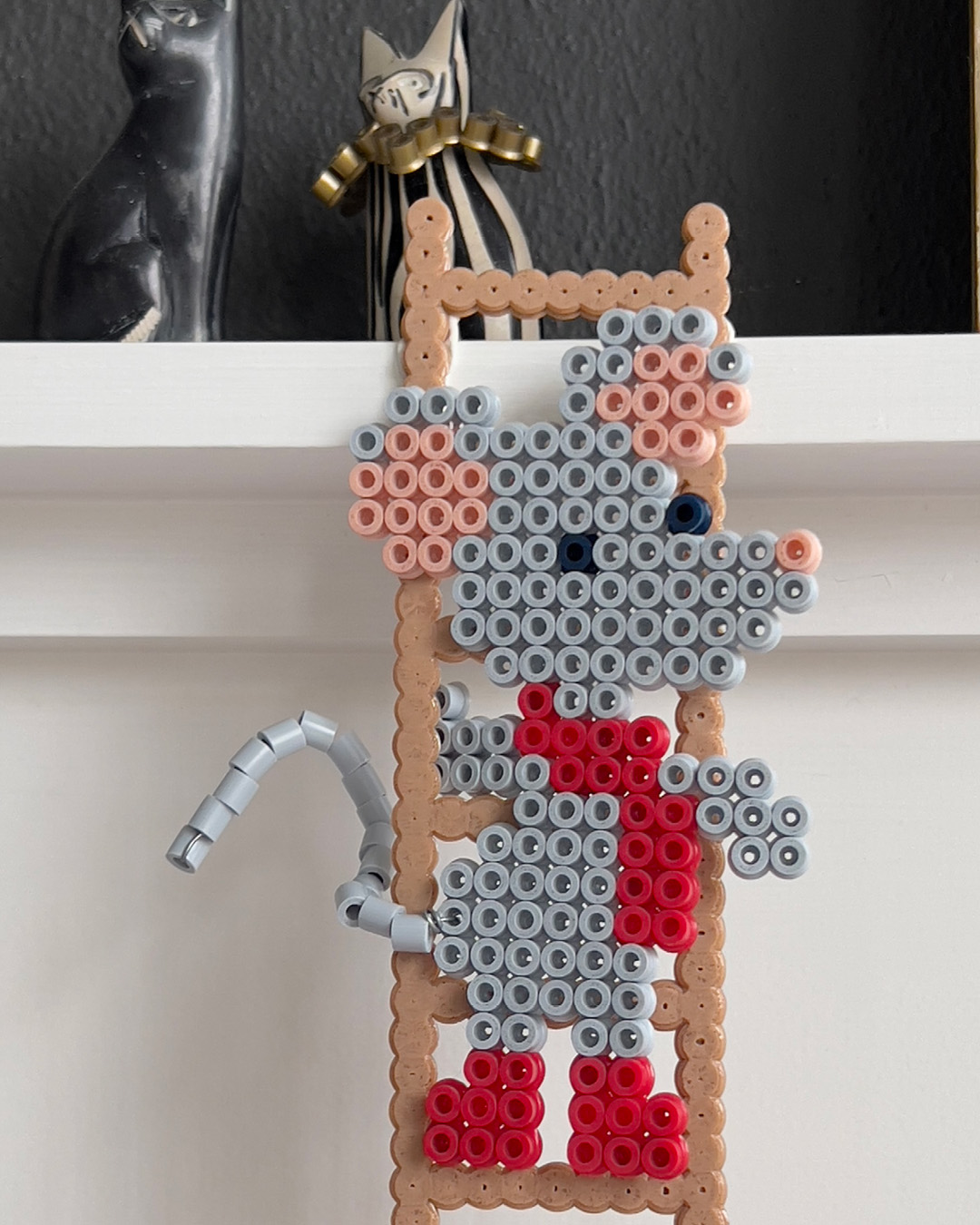 Hama-perlemus i grått og rødt festet på en brun perlestige.