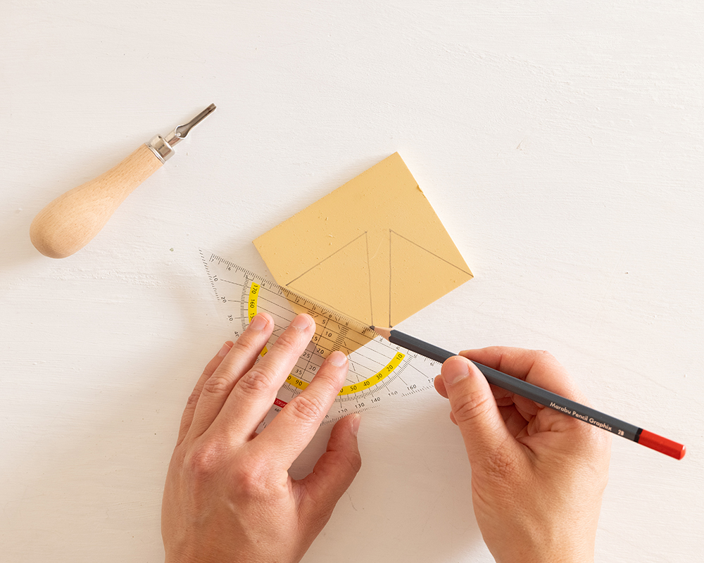 Hender som tegner trekantformer på en lys gummiplate ved hjelp av linjal og blyant.