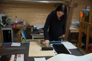 Kvinne påfører trykksverte på en tresnittplate med en rulle i et verksted.