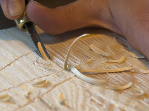 Hender skjærer i en tresnittplate med et lite jern.