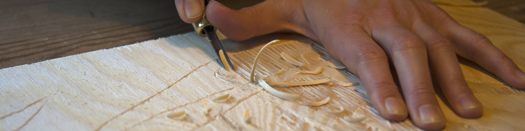 Hender skjærer i en tresnittplate med et lite jern.