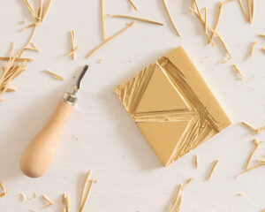 Utskåret gummiplate med trekantmønster og treskjæreverktøy på lys bordflate.