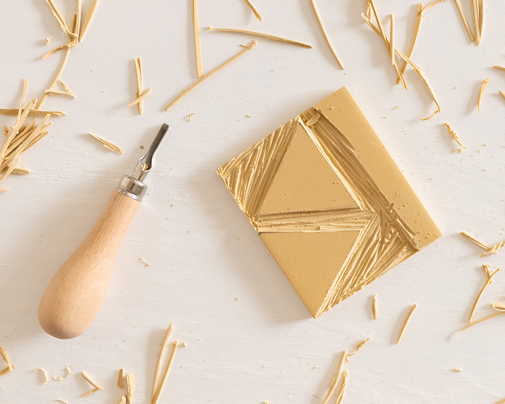 Utskåret gummiplate med trekantmønster og treskjæreverktøy på lys bordflate.