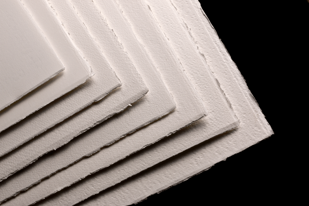 Stabler av Fabriano akvarellpapir med håndrevne kanter mot mørk bakgrunn.