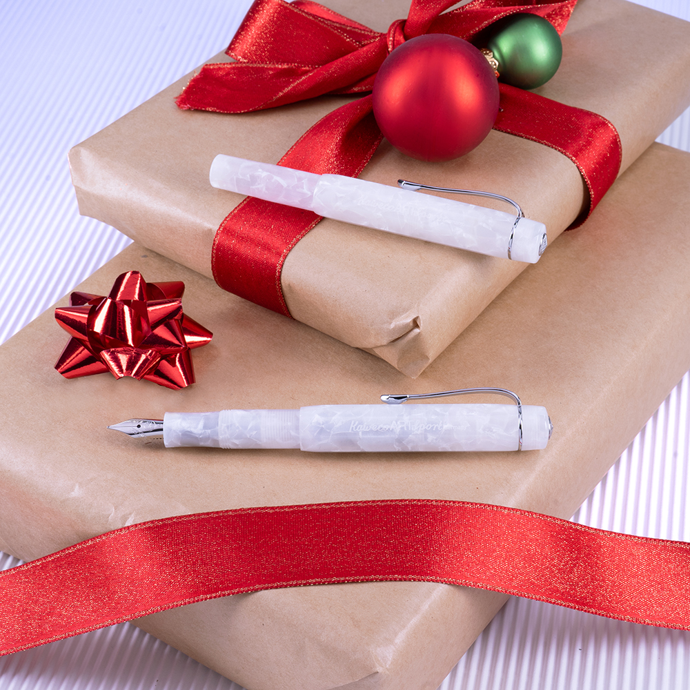 Hvite Kaweco-penn­er på brunt gavepapir med røde bånd og julekuler.