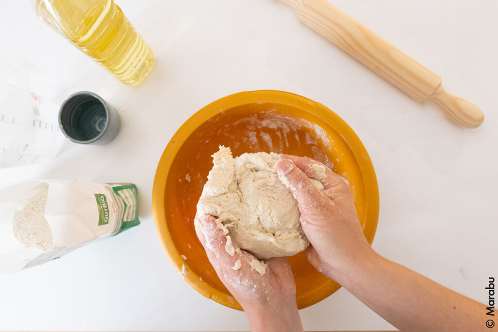 Hender som knar lys trolldeig over en oransje bolle.