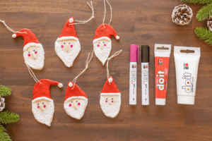 Seks håndlagde nisser i trolldeig med snor, arrangert på trebord sammen med tusjer og maling.
