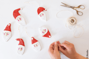 Håndlagde figurer i trolldeig formet som nisser med snor til oppheng, lagt på hvit bakgrunn.