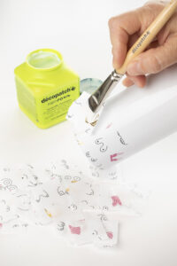 Pensel påfører decoupagelim på papir rundt et glass.