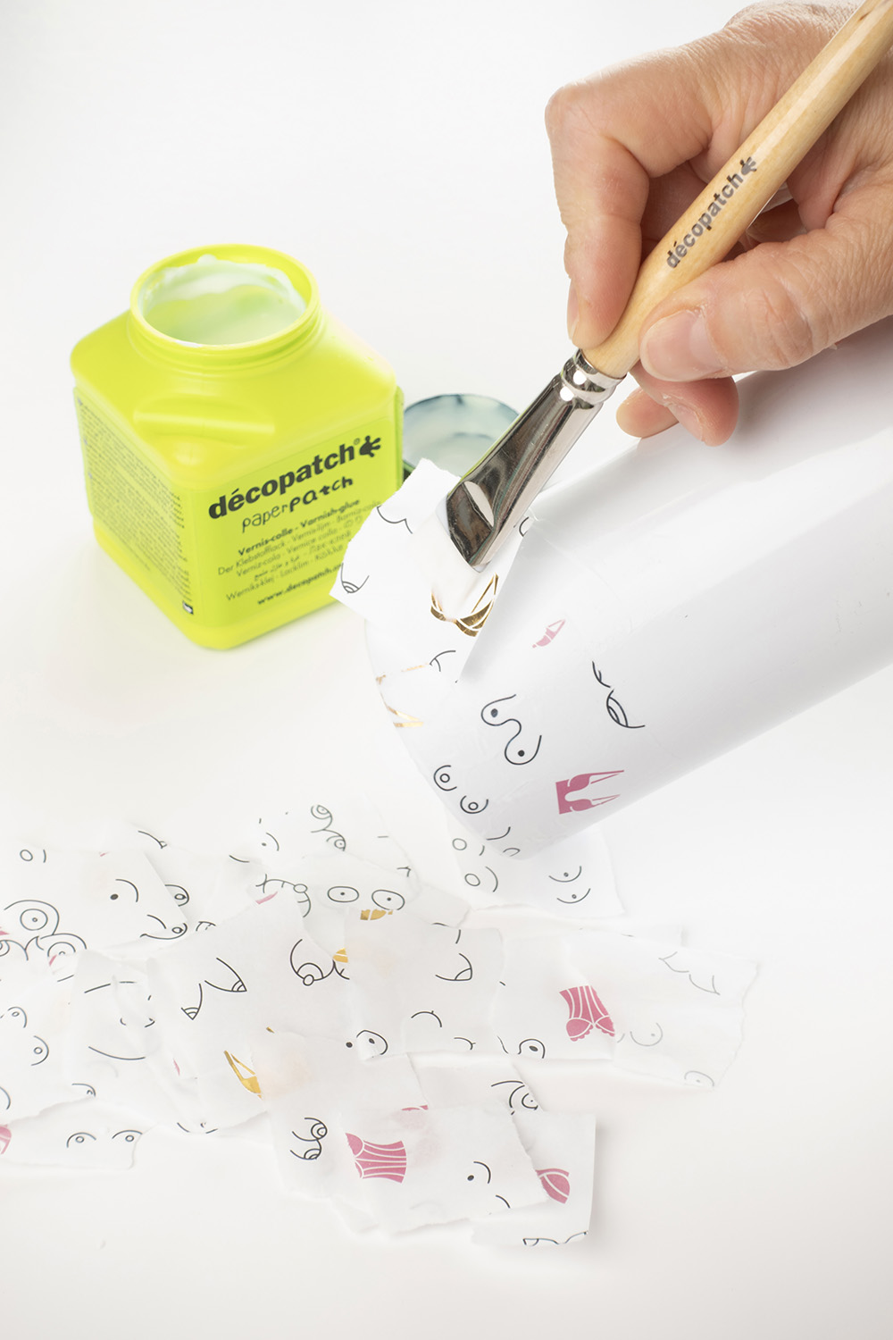 Pensel påfører decoupagelim på papir rundt et glass.