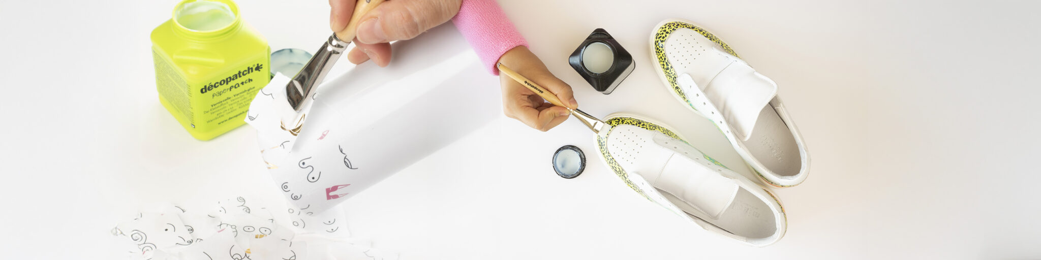 Hånd bruker pensel og decoupagelim på papir og hvite sneakers.