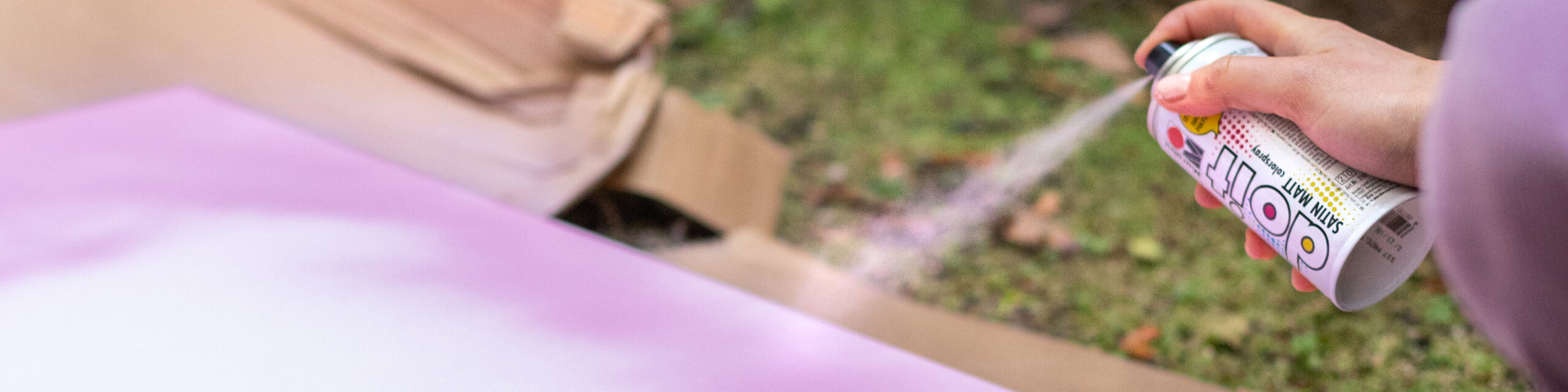 Hånd som spraymaler rosa flate med sprayboks utendørs.