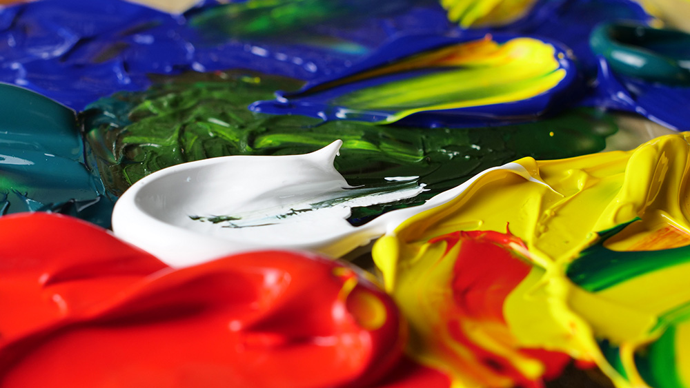 Tykk akrylmaling i rødt, gult, blått, grønt og hvitt i nærbilde.