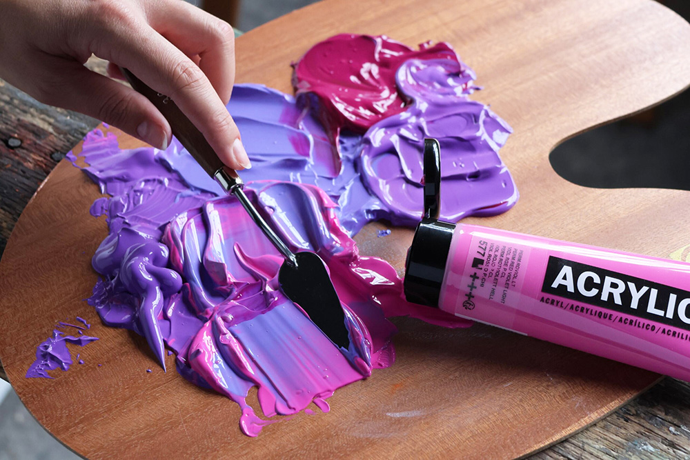Hånd med palettkniv blander lilla og rosa Amsterdam ACRYLIC maling på trepalett.
