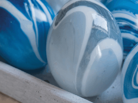Blå og hvite marmorerte påskeegg i en grå brettform, med små prestekrager rundt.