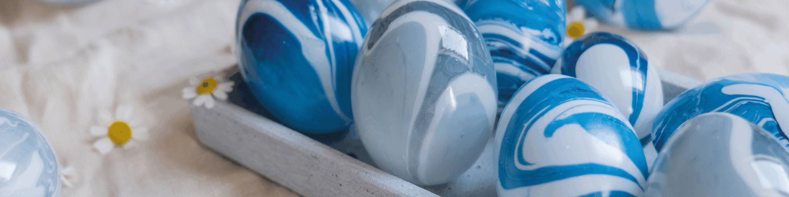 Blå og hvite marmorerte påskeegg i en grå brettform, med små prestekrager rundt.