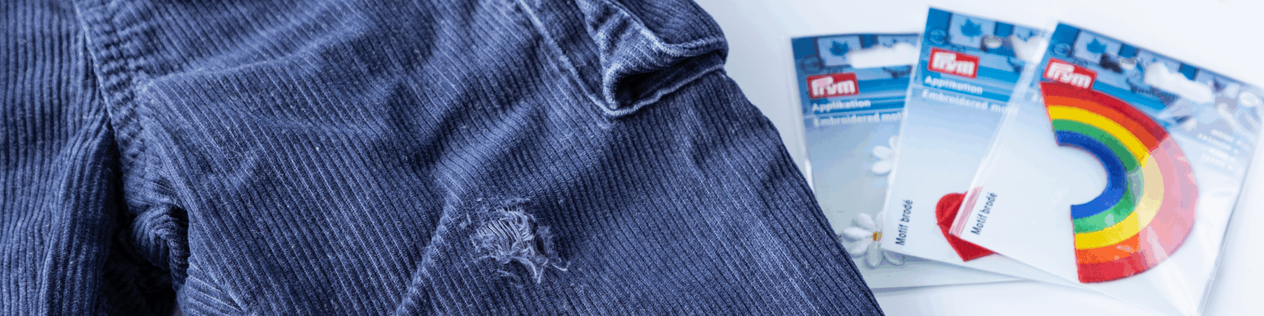 Blå kordbukse med hull ved siden av Prym reparasjonslapper i emballasje.